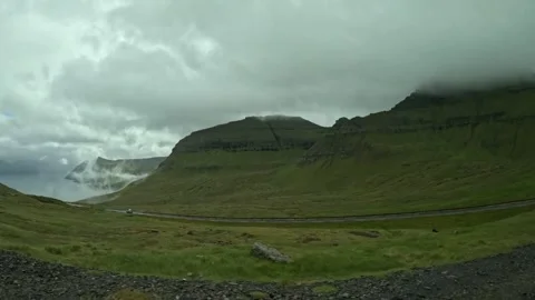 White car driving on a winding mountain road under cloudy sky, Faroe Islands Stock Footage 340005300