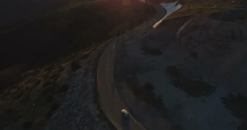 White car driving on winding remote mountain road. Sunset lights shine over Stock Footage 129882879