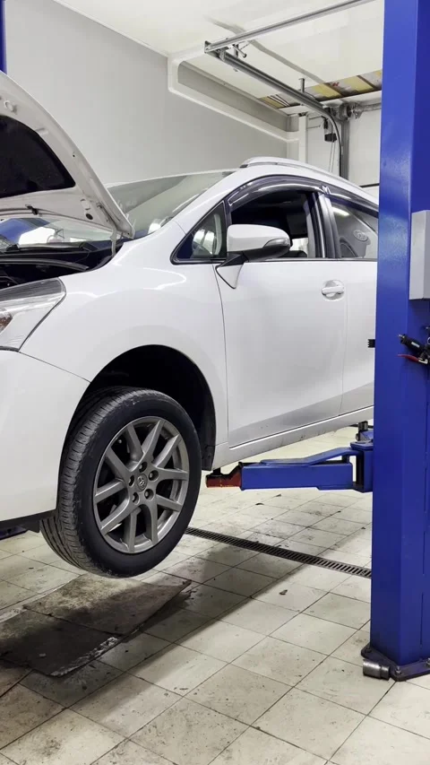 A white car is elevated on a hydraulic lift in a garage. The hood is open Stock Footage 318829803