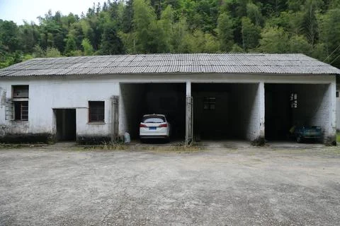 White car parked inside weathered open garage bay beside old building and w.. Foto stock