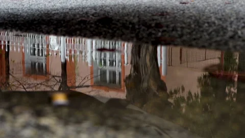 A white car passing on the road is reflected in the puddle under the parked car Vídeo Stock 221909885