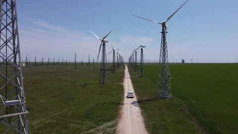 White car rides on an empty sandy road in a field past huge windmills Stock Footage 155608663