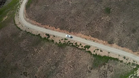 White car taking a corner on curvy dirt road in vast plains Stock Footage 131719564