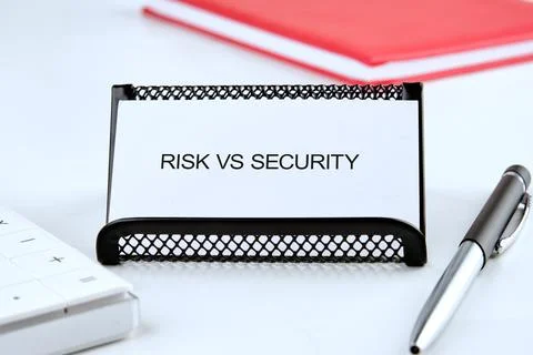 A white card reading risk versus security sits in a black holder on a white d Stock Photos
