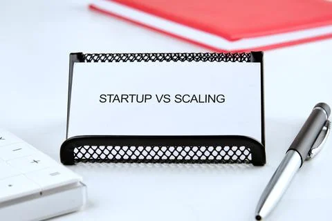 A white card reading Startup VS Scaling sits in a black holder on a white des Stock Photos
