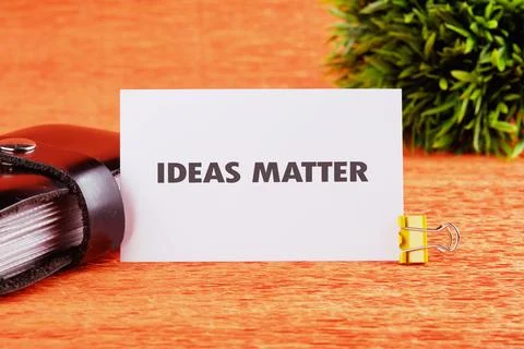 A white card stating IDEAS MATTER sits with a gold clip next to a black book Stock Photos