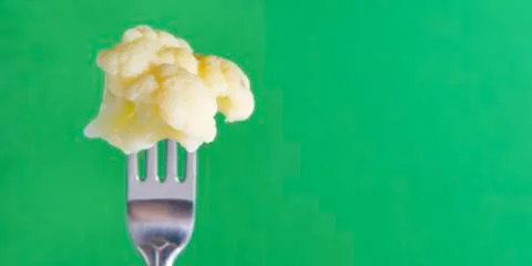 White cauliflower on a fork on a green background, vegetable Foto stock
