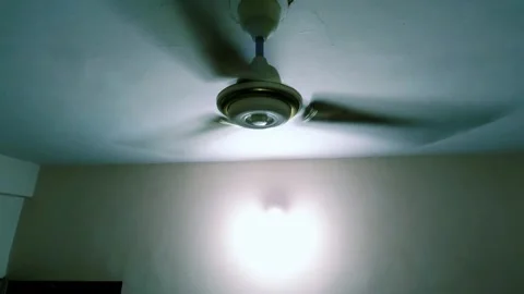 A white ceiling fan spins at maximum speed inside an overcrowded community cente 스톡 동영상 343784175