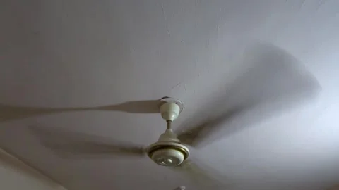 A white ceiling fan spins at maximum speed inside an overcrowded community cente Stock Footage 343784182