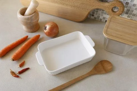 White ceramic baking dish with fresh carrots and onion on kitchen counter. Stock Photos