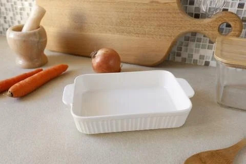 White ceramic baking dish with fresh carrots and onion on kitchen counter. Stock Photos