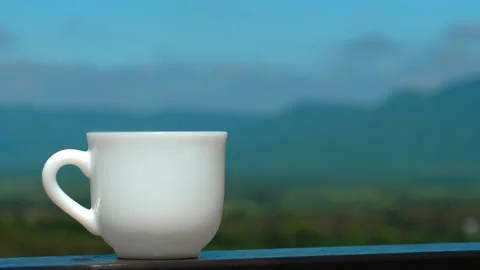 White ceramic coffee cup placed on wooden table against backdrop of Stock Footage 275611825
