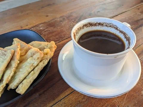 White ceramic cup of hot black coffee and fried tempeh or tempeh mendoan on.. Stock Photos