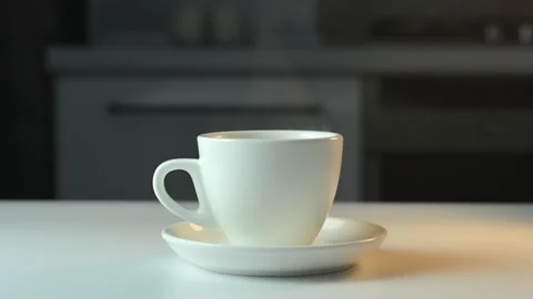 White ceramic cup with hot coffee tea on saucer stands on white table against Stock Footage 198477179
