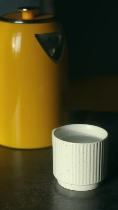White ceramic cup with hot steam and yellow kettle Video stock 323896855