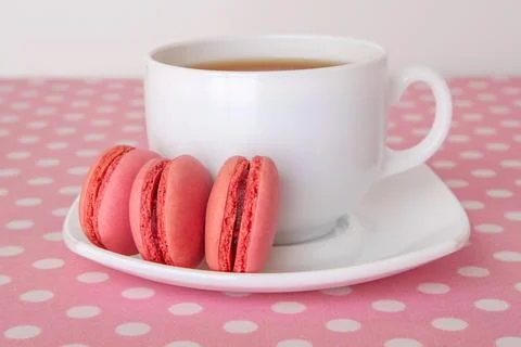 White ceramic cup with tea and sweet pink macarons on a plate over polka dot  Stock Photos