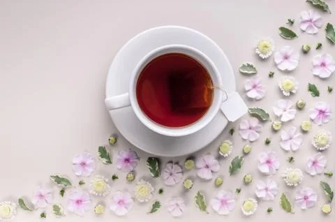 White ceramic cup with tea on a corner floral pattern on a beige background.  Stock Photos