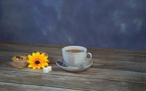 A white ceramic cup with tea, next to a napkin are two cupcakes with sugar cu Stock Photos