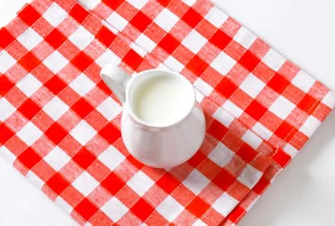 White ceramic milk jug on red checkered cloth Stock Photos