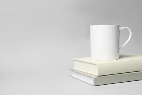 White ceramic mug and stack of books on light background, space for text Stock Photos