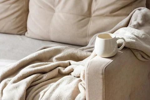 White ceramic mug on plush sofa with cozy blanket Stock Photos