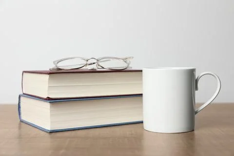 White ceramic mug, stack of books and glasses on wooden table Stock Photos