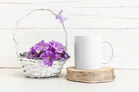 White ceramic mug on the table with a basket of flowers. 写真素材