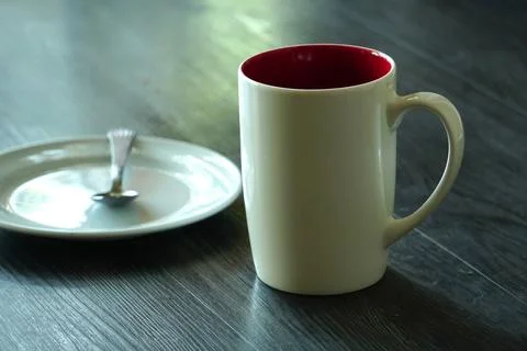A white ceramic mug with a vibrant red interior sits next to a small plate. Stock Photos