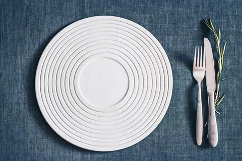 White ceramic plate with fork and knife on blue textile tablecloth minimal Stock Photos