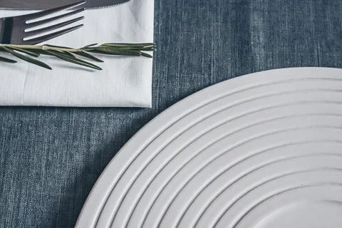 White ceramic plate with fork knife and rosemary on blue textile table Stock Photos