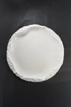 White ceramic plate with rough textured rim on dark textile background Stock Photos