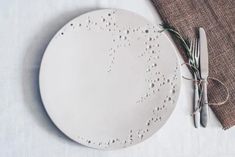 White ceramic plate with textured pattern fork knife rosemary and linen Stock Photos