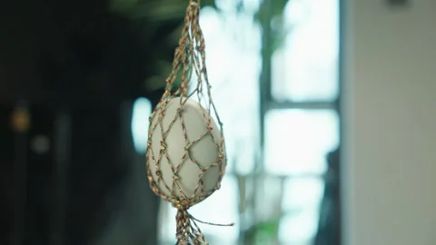 White Ceramic Pot Hanging in Colorful Macrame Net Near Window Видео 339069166