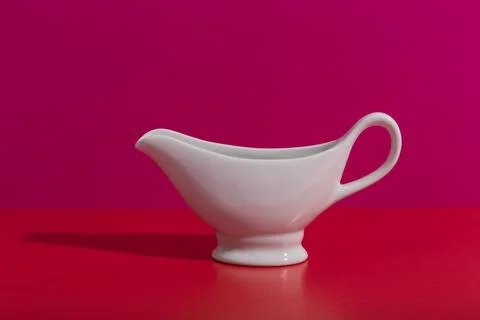 White ceramic sauce boat on creative red and pink background with space for text Stock Photos