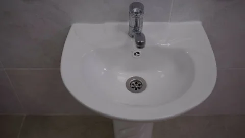 White ceramic sink with chrome faucet showing water flow in a modern bathroom 스톡 동영상 336063308
