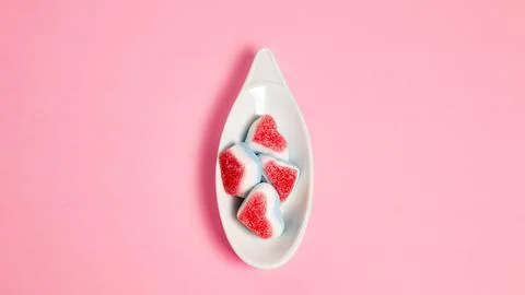 White ceramic spoon with candies in the shape of hearts on a pink background Stock Photos
