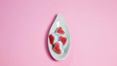 White ceramic spoon with candies in the shape of hearts on a pink background Foto stock