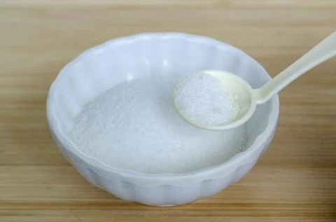 White ceramic spoon scooping salt from bowl highlighting sodium measurement.. Stock Photos