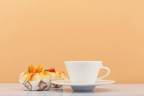 White ceramic tea or coffee cup with pastry next to it against beige background Stock Photos