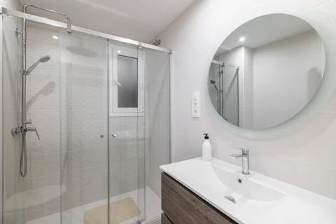 White ceramic tile bathroom with large round mirror on the wall reflecting the Stock Photos