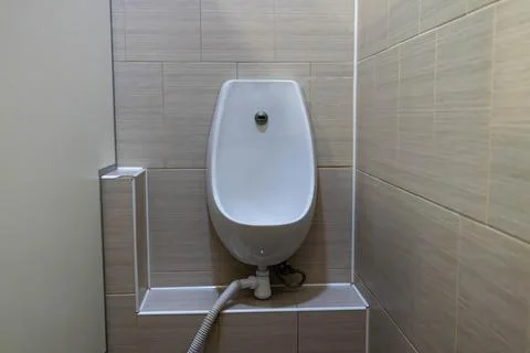 White ceramic urinal mounted on tiled wall in public toilet Stock Photos