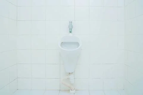 White ceramic urinal mounted on a tiled wall in a restroom, featuring a flush Stock Photos