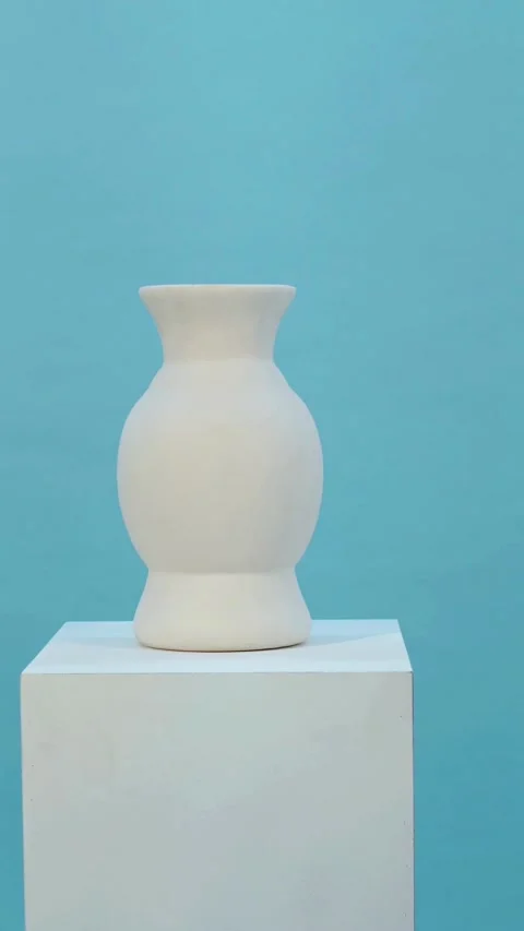 White ceramic vase sitting on white pedestal against blue Stock Footage 331773767