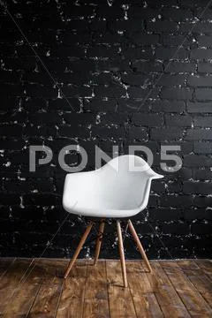 White chair standing in room on brown wooden floor over black brick wall Stock Photos