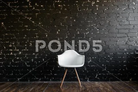 White chair standing in room on brown wooden floor over black brick wall Stock Photos