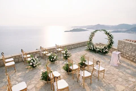 White chairs stand in rows in front of a wedding arch and reception table on an Stock Photos