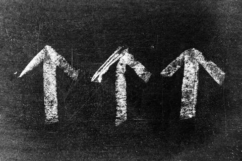 White chalk drawing as arrow shape on black board background Stock Photos