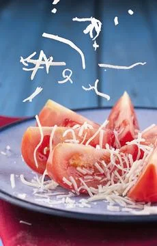 White cheese falling on tomato slices. Stock Photos
