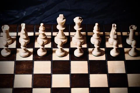 White Chess Pieces Lined Up in Front View on Wooden Board Against Dark Back.. Stock Photos