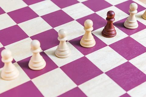 White chess sets lined up and a black pawn between them on a wooden chessboard Stockfoto's
